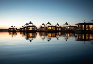 Floating Village Brombachsee-Lodges in Baviera al tramonto, illuminati e riflessi sull’acqua calma.