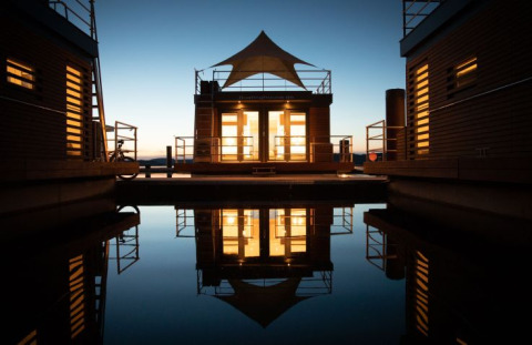 Hébergement glamping au Floating Village Brombachsee, Bavière, éclairé au crépuscule et reflété sur l'eau.
