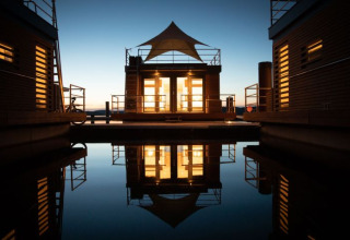 Alojamiento glamping en Floating Village Brombachsee, Baviera, iluminado al anochecer reflejado en el agua.