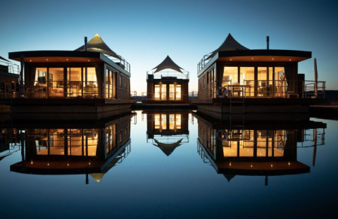 Floating Village Brombachsee glamping lodges in Bavaria, illuminated at dusk and reflected in calm water.