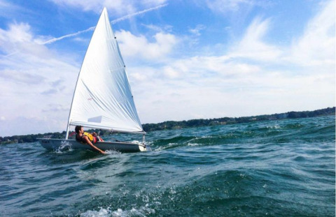 Un voilier avec une personne navigue près du Floating Village Brombachsee - Lodges Bayern sous ciel bleu.