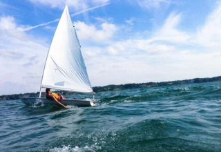 En sejlbåd med én person sejler på bølgerne under blå himmel nær Floating Village Brombachsee - Lodges Bayern.