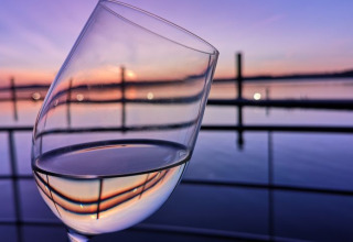 Wijnglas met uitzicht op een rustige meer bij zonsondergang, Floating Village Brombachsee - Lodges Bayern.