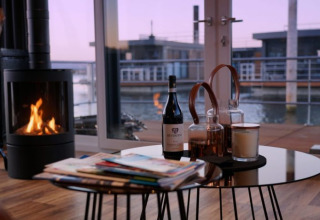 Escena interior de Floating Village Brombachsee - Lodges Bayern con chimenea, vino y vista al agua.