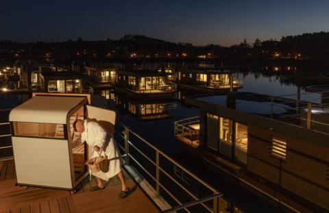 Floating Village Brombachsee lodges op het meer ’s nachts met persoon in badjas bij een buitensauna.