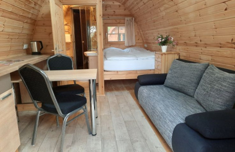 Interior view of a wooden pod at Campotel Nord-Ostsee in Schleswig-Holstein with sofa and bed.