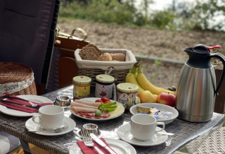 Table de petit-déjeuner en plein air avec pain, fruits, charcuterie et café au Campotel Nord-Ostsee, Schleswig-Holstein.
