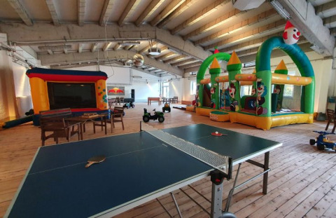 Area giochi interna con tavolo da ping-pong, tavoli, sedie e castelli gonfiabili al Campotel Nord-Ostsee.