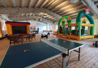 Indoor play area with table tennis, tables, chairs, and inflatable bouncy castles at Campotel Nord-Ostsee.