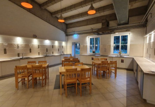 Cocina comunitaria moderna en Campotel Nord-Ostsee - Pods Schleswig-Holstein con mesas de madera y ventanas grandes.