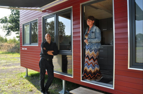 Deux personnes devant une tiny house rouge à Klein vakantie- en tentoonstellingspark, glamping en Basse-Saxe.