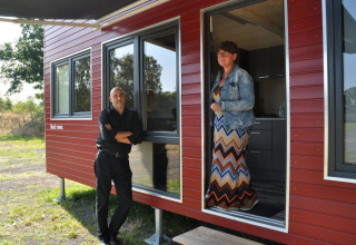Zwei Personen stehen vor einem roten Tiny House im Klein vakantie- en tentoonstellingspark, Glamping Niedersachsen.