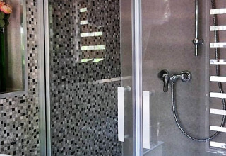 Modern bathroom with mosaic tiles, glass shower door, and handheld shower at glamping in Lower Saxony.