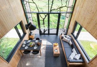 Interno moderno di casa sull'albero glamping con grandi finestre, tavolo da pranzo e divano con vista sul verde.