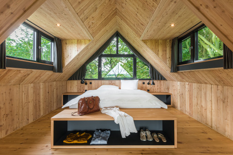 Cozy bedroom in a luxury glamping treehouse lodge with wood walls, natural light, and scenic windows.