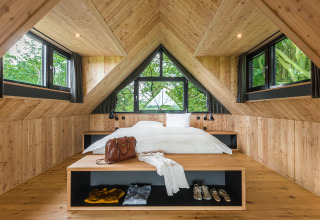 Cozy bedroom in a luxury glamping treehouse lodge with wood walls, natural light, and scenic windows.