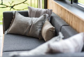 Sfeervolle glampingbank met kussens in Lütetsburg Lodges - Boomhutten Nedersaksen, bij het raam.