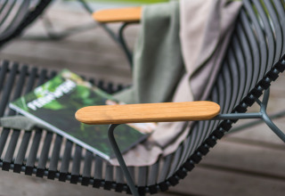 Modern outdoor chair with wooden armrests, blanket and magazine on deck at Lütetsburg Lodges - Boomhutten Nedersaksen