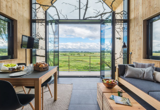 Alojamiento glamping moderno con grandes ventanales, vistas a campos verdes y decoración acogedora.