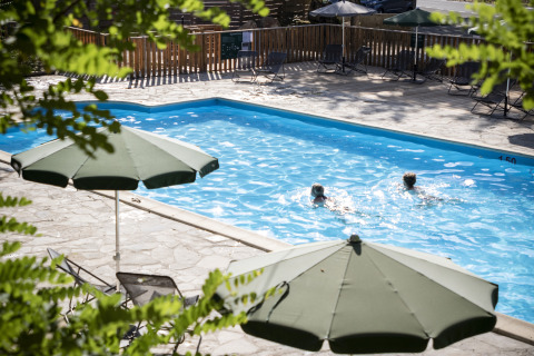 Außenpool mit zwei Schwimmern und grünen Sonnenschirmen im Huttopia Gorges du Tarn, Glamping Midi-Pyrénées.