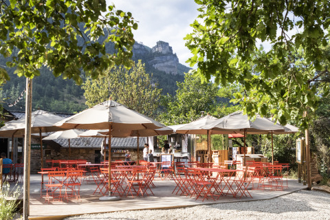 Outdoor café with red chairs and umbrellas at Huttopia Gorges du Tarn, glamping site in the Midi-Pyrénées.