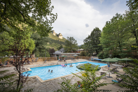 Piscine extérieure entourée d’arbres et de montagnes à Huttopia Gorges du Tarn Glamping en Midi-Pyrénées.