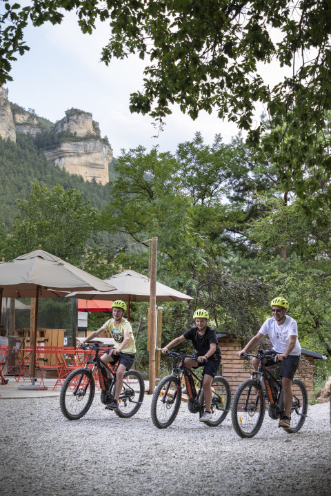 Tre persone pedalano con caschi gialli davanti al glamping Huttopia Gorges du Tarn nelle Midi-Pyrénées.