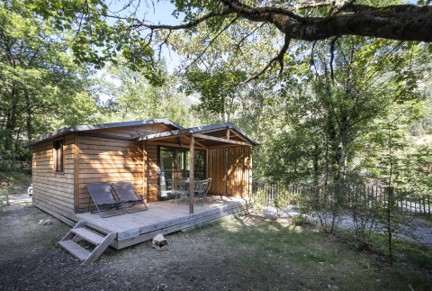 Cabaña de madera tipo glamping en Huttopia Gorges du Tarn, rodeada de árboles en Midi-Pyrénées, Francia.