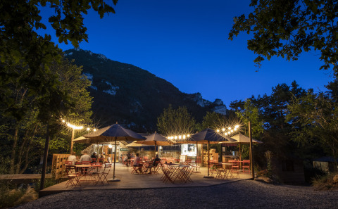 Zona de comedor al aire libre con luces y sombrillas en Huttopia Gorges du Tarn glamping en Midi-Pyrénées, Francia.