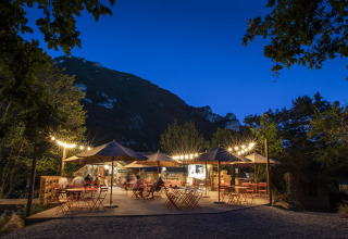 Buiten eetgedeelte met lichtslingers en parasols bij Huttopia Gorges du Tarn glamping in Midi-Pyrénées, Frankrijk.