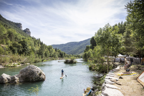 Person paddleboarding on a river at Huttopia Gorges du Tarn glamping site in Midi-Pyrénées, surrounded by mountains.