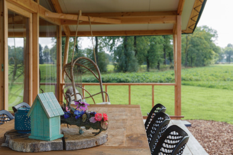 Terrasse couverte au Glamping - Landrijk de Reesprong avec table en bois, déco et vue sur les champs verts.