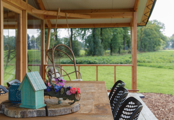 Veranda coperta al Glamping - Landrijk de Reesprong con tavolo rustico e vista sui campi verdi circostanti.