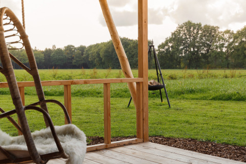 Vue d'une terrasse en bois chez Glamping - Landrijk de Reesprong, donnant sur une pelouse et un champ vert.