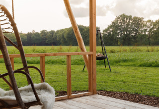 Vista desde un porche de madera en Glamping - Landrijk de Reesprong, con césped verde y campo al fondo.
