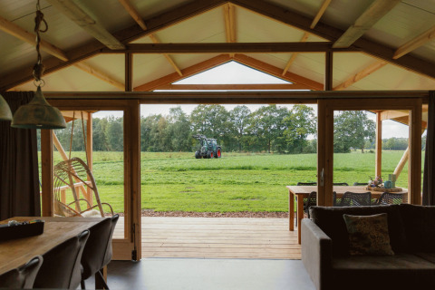 Vue depuis un hébergement glamping à Landrijk de Reesprong, terrasse couverte et tracteur au champ.