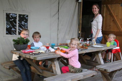 Gezin eet samen aan een picknicktafel bij een glamping tent op Landrijk de Reesprong in Nederland.