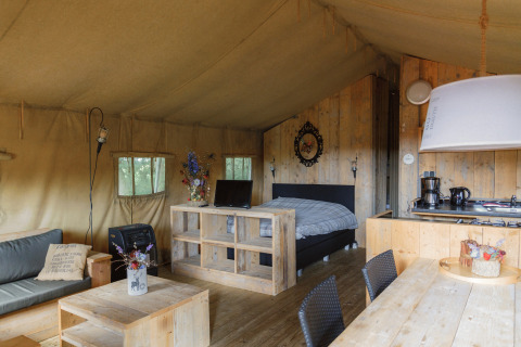 Gemütliches Glamping-Zelt bei Landrijk de Reesprong mit Bett, Küche, Sofa und Essbereich aus Holz.