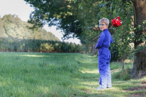 Niño con mono azul y gafas pasea por la naturaleza en Glamping - Landrijk de Reesprong con un palo y atillo.