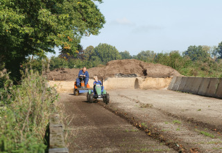 Un père et son enfant roulent en mini-tracteurs à Glamping - Landrijk de Reesprong, entourés de nature.