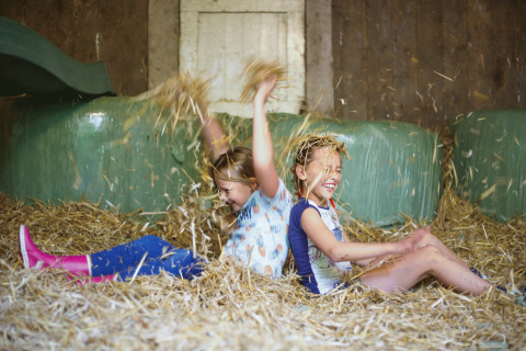 Twee lachende kinderen spelen in stro bij Glamping - Landrijk de Reesprong, omringd door hooibalen.