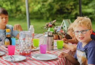 Kinderen genieten van een maaltijd buiten bij Glamping - Landrijk de Reesprong, aan tafel met rood geruit kleed.