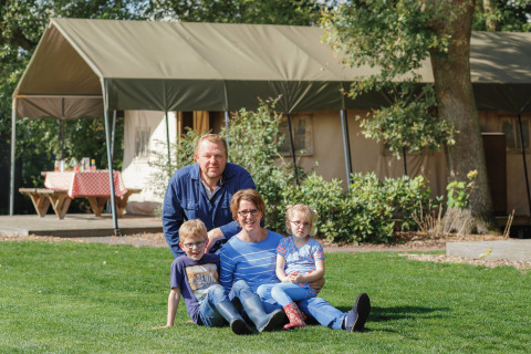 Familia sentada en el césped frente a su tienda glamping en Landrijk de Reesprong, disfrutando de la naturaleza.