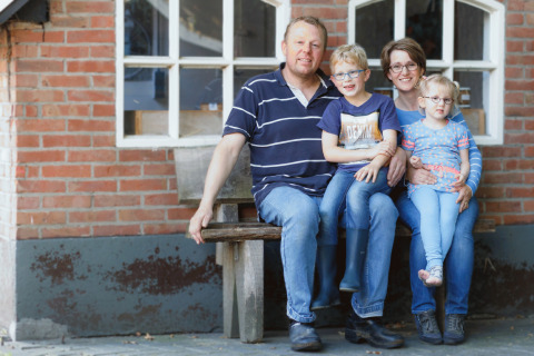 A family of four sits smiling on a bench outside a brick building at Glamping - Landrijk de Reesprong.