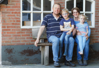 A family of four sits smiling on a bench outside a brick building at Glamping - Landrijk de Reesprong.