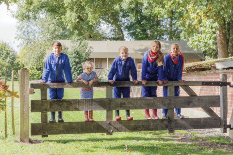 Vijf kinderen in blauwe overalls staan op een houten hek bij Glamping Landrijk de Reesprong in Nederland.