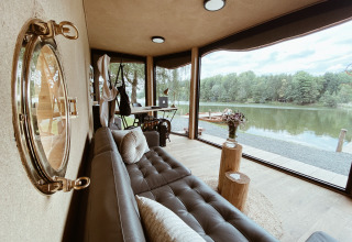 Modernes Glamping-Apartment am See mit großen Fenstern, stilvollem Sofa und herrlichem Naturblick.