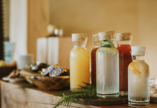 Assorted juice bottles with cork lids arranged on a rustic table at Falkensteiner Blaguš glamping.