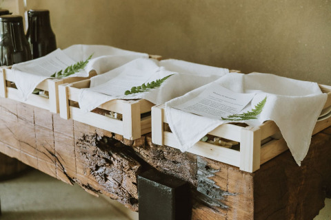 Vassoi di legno con tovaglioli, menu e foglie di felce su un tavolo rustico al Falkensteiner Premium Camping Blaguš.
