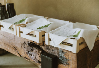 Vassoi di legno con tovaglioli, menu e foglie di felce su un tavolo rustico al Falkensteiner Premium Camping Blaguš.